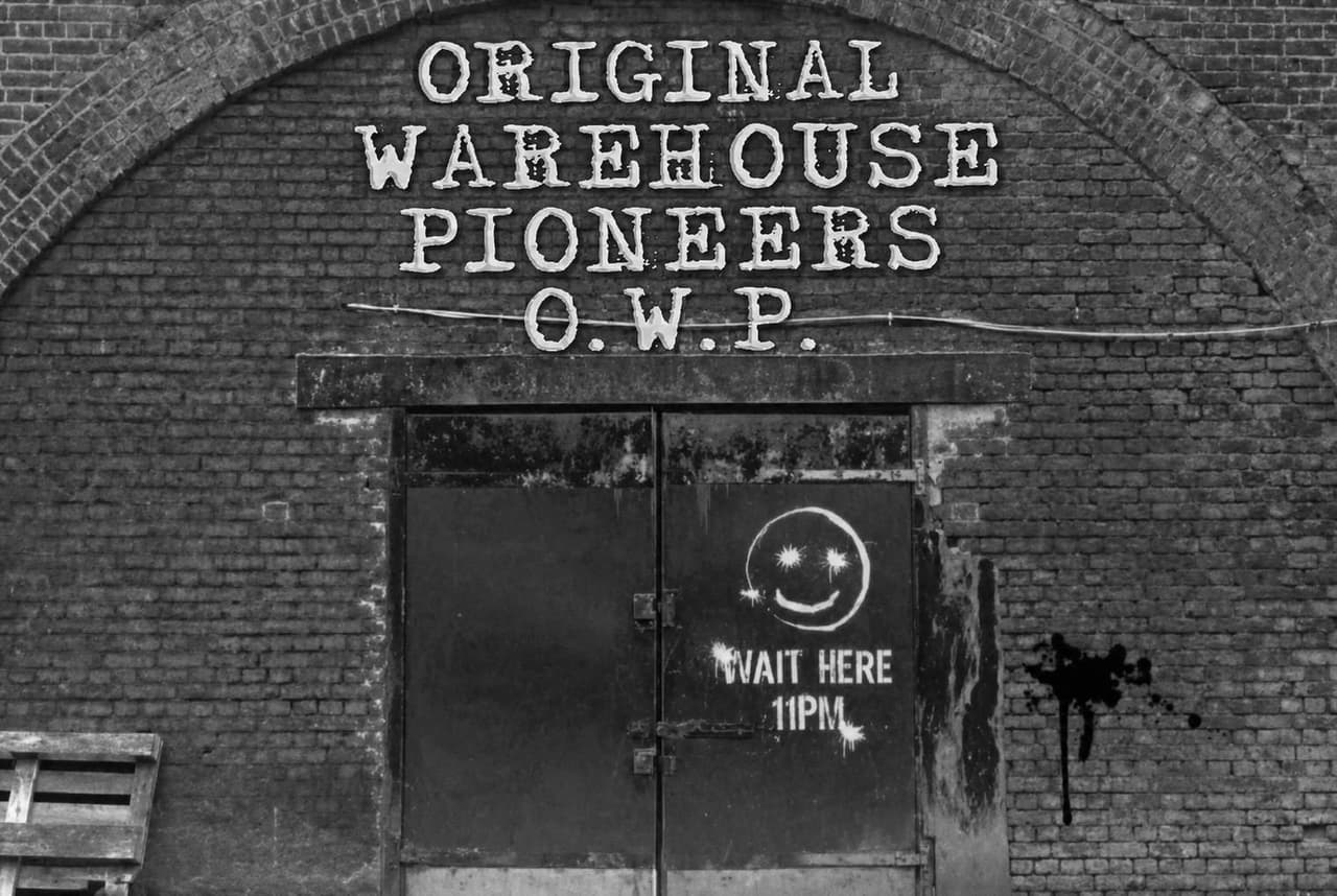 A Manchester railway arch, the words 'Original Warehouse Pioneers - O.W.P.' painted above the doors, and an acid-house smiley face beside the instruction 'Wait here 11pm.'